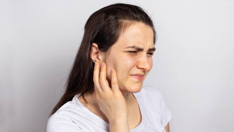 Person holding their jaw, illustrating common symptoms of TMD and facial pain.
